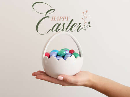 Easter greeting card with female hand holding basket of chocolate eggs