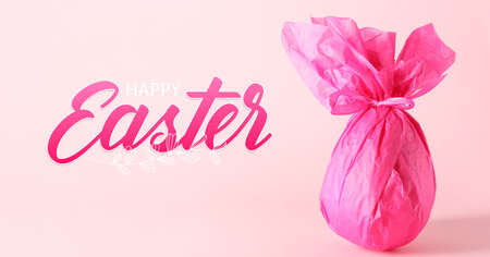 Chocolate egg wrapped in pink paper and text EASTER on color backgroundの写真素材
