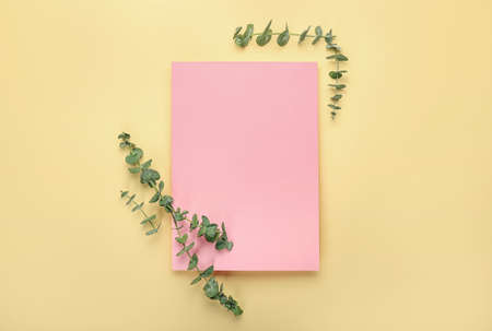 Blank sheet of paper and fresh eucalyptus branches on color background