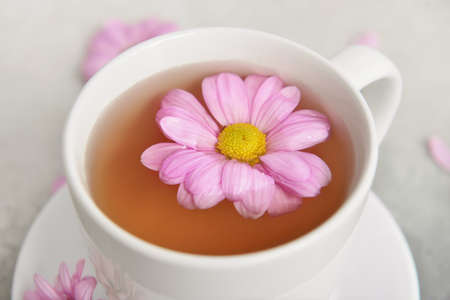 Cup of floral tea with flower on light background, closeup