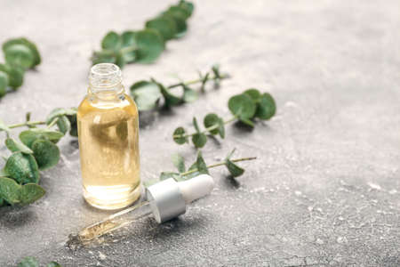 Bottle of essential oil and fresh eucalyptus branches on grunge background, closeupの写真素材