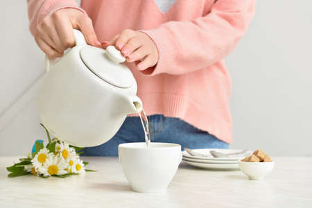 Woman pouring tea from teapot into cup on tableの写真素材
