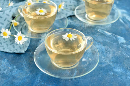 Cups of floral tea with chamomile flowers on color background
