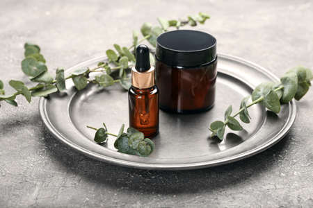 Plate with cosmetic products and eucalyptus branches on grunge backgroundの写真素材