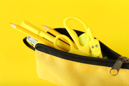 Pencil case with stationery on yellow background, closeup