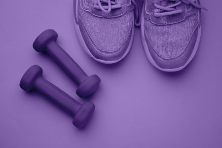 Dumbbells and shoes on violet background with space for text, top viewの写真素材