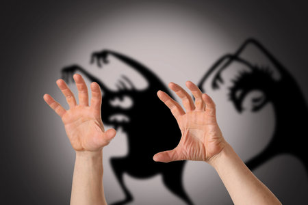 Hands of scared man and silhouettes of monsters on gray background. concept of fear and nightmare