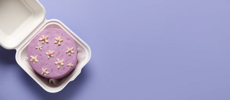 Lunch box with tasty bento cake on lilac background with space for textの写真素材