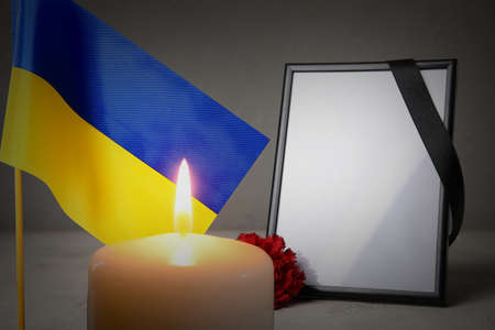 Blank funeral frame, flag of Ukraine and burning candle on gray background. Honoring the fallen...