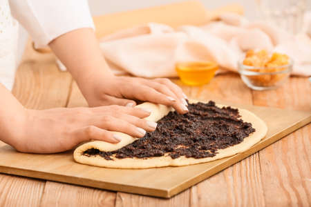 Woman preparing tasty poppy seed bun at table in kitchen