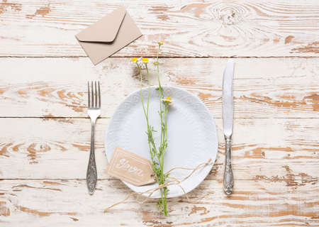 Beautiful table setting with chamomile flowers and envelope on white wooden background