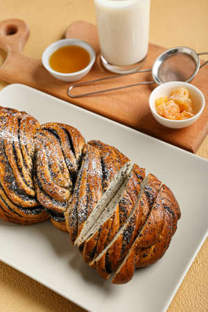 Plate with tasty poppy seed bun on color background