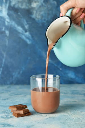 Pouring of delicious chocolate milk from jug into glass on color backgroundの写真素材