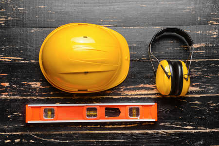 Hardhat with ear protectors and builder's level on dark wooden background
