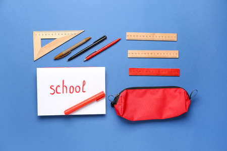 Paper with word SCHOOL and stationery on color background