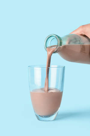 Pouring of delicious chocolate milk from bottle into glass on color background