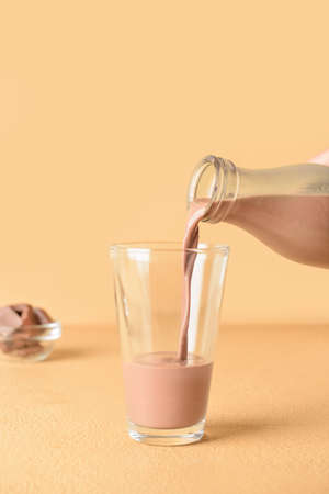 Pouring of delicious chocolate milk from bottle into glass on color backgroundの写真素材