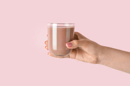 Female hand holding glass of delicious chocolate milk on color backgroundの写真素材