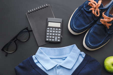 Stylish school uniform, shoes, eyeglasses and stationery on dark background, closeup