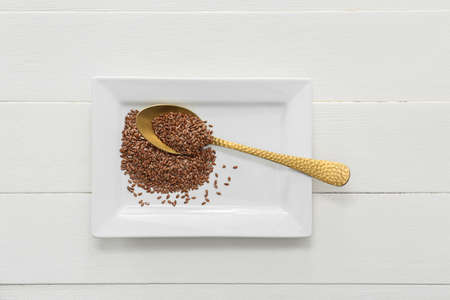 Plate with flax seeds on light wooden background