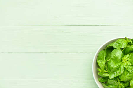 Bowl with fresh basil leaves on color wooden background