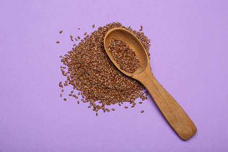 Spoon with flax seeds on color background