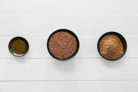 Bowls with flax seeds and oil on light wooden background