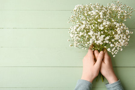Female hands with beautiful gypsophila flowers on color wooden backgroundの写真素材
