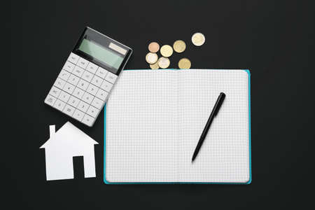 Paper house with notebook, calculator and coins on black backgroundの写真素材