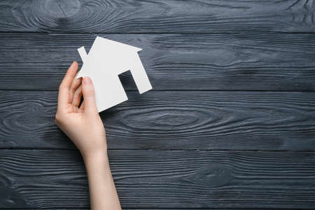 Female hand and wooden house on dark wooden background. real estate conceptの写真素材