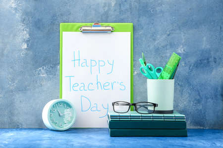 Clipboard with text HAPPY TEACHER'S DAY, alarm clock and stationery on color background