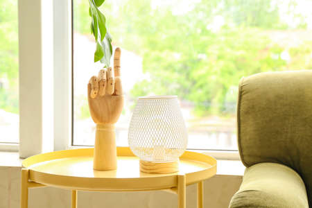Wooden hand and modern lamp on table near big window