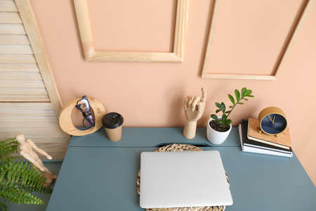Modern laptop, wooden hand and cup of coffee on color table