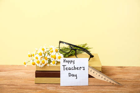 Eyeglasses with flowers, books and sticker note on table near color wall