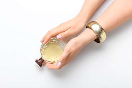 Woman with beautiful manicure and stylish jewelry holding perfume bottle on white background
