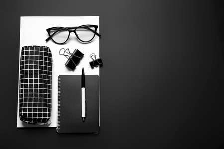 Stylish pencil case, eyeglasses and stationery on dark background