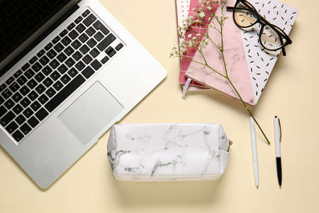 Stylish pencil case, eyeglasses, laptop and stationery on color background, closeup
