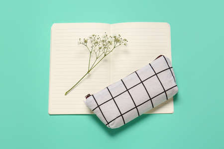 Pencil case, notebook and flowers on color background