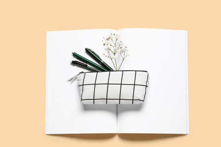 Stylish pencil case with pens and notebook on color background