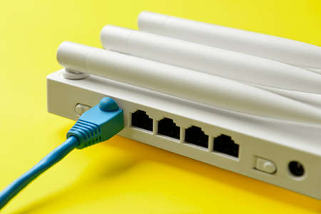 WiFi router with antennas and network cable on color background