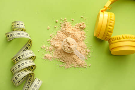 Scoop with protein powder, measuring tape and headphones on color background, closeup