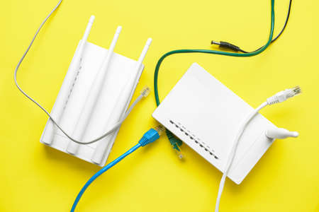 Wi-Fi router with antennas and network cables on color background