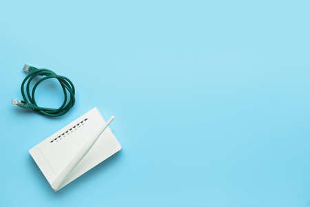 Wi-Fi router with antenna and network cable on color background