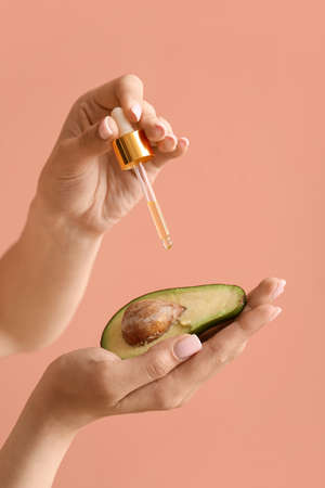 Woman dripping essential oil on fresh avocado against color background, closeupの写真素材