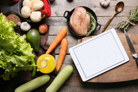 Tablet computer with fresh vegetables and raw chicken meat on dark wooden tableの写真素材