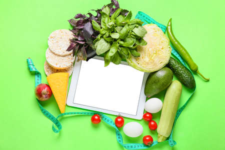 Tablet computer with blank screen, healthy products and measuring tape on green backgroundの写真素材
