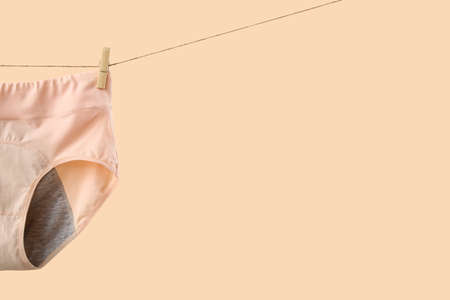 Period panties hanging on clothesline against color background