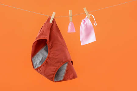 Period panties, menstrual cup and bag hanging on rope against color backgroundの写真素材