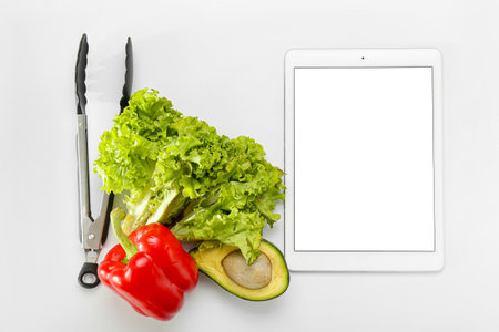 Digital recipe book, tongs, lettuce, avocado and bell pepper on white backgroundの写真素材