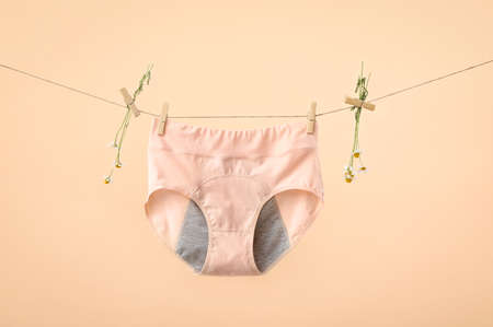 Period panties and chamomile flowers hanging on rope against color background